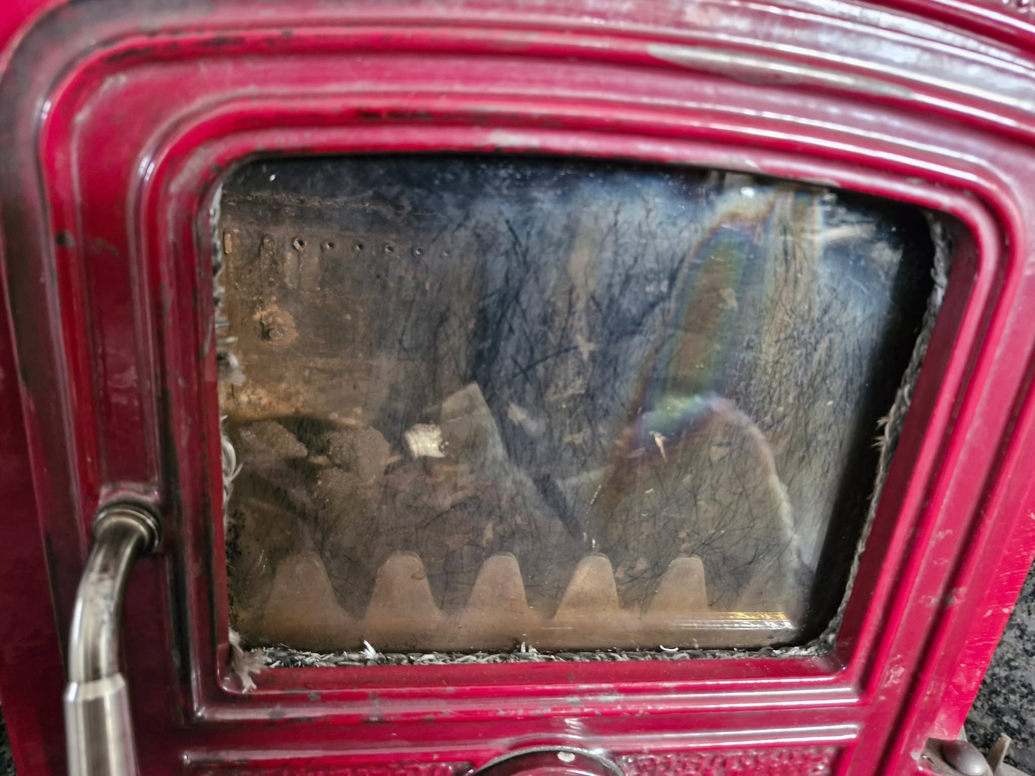 The sooted glass door of a red enamel stove